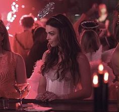 two women sitting at a bar with candles in front of them, one wearing a tiara