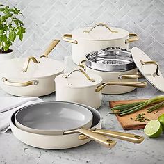 white pots and pans with gold handles are sitting on a counter next to limes