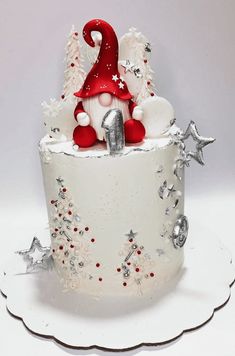 a white cake with red and silver decorations on it's side, topped with a gnome figurine