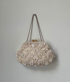 This is a beautiful vintage 1960s beaded white flower purse! It is a snap purse with one compartment inside, white satin lining, and gold hardware. This bag is covered in lovely white beads that shimmer and turn a slight pink shade in the light. It was hand made in Hong Kong in the 60s. It is turly a unique and timeless piece! Tag: Hand Made in Hong Kong Materials: White beads, gold hardware and satin lining. Measurements: Length: 8.5" Width: 1" Strap: 6" Condition: Great! All beads in place, just a few light marks on the inside lining and slight fading on gold strap (as pictured). Vintage 1960s white beaded floral purse, Vintage hand made in Hong Kong beaded wrist strap purse, 1960s beaded formal evening pursed Vintage Formal Clutch With Pearl Handle, Vintage White Clutch Evening Bag, Vintage Pearl Handle Clutch Evening Bag, Vintage Evening Clutch With Pearl Handle, Vintage White Pouch Evening Bag, Vintage Cream Clutch Bag, Vintage Evening Bag With Pearl Embroidery For Events, Vintage Pearl Embroidered Evening Bag For Events, Vintage Cream Bags For Weddings