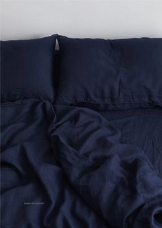 an unmade bed with dark blue sheets and pillow cases on it's side