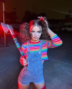 a woman in overalls holding a large knife and posing for the camera with her hands behind her head