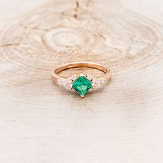 an emerald and diamond ring sitting on top of a piece of wood