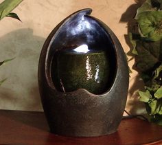 a green vase sitting on top of a wooden table next to a potted plant