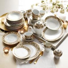 a table topped with lots of white and gold dinnerware next to a vase filled with flowers