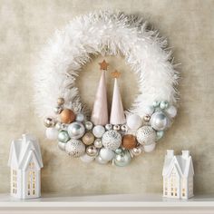 a christmas wreath with ornaments on top of it next to small white houses and trees