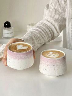 two cups of coffee on a table with one being held by someone's hand