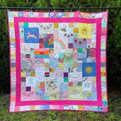 a pink and white quilt hanging on a fence next to some bushes with trees in the background