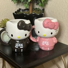 two hello kitty figurines sitting on top of a table next to a potted plant