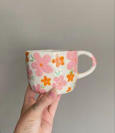 a hand holding up a pink and orange flowered coffee cup with white rims