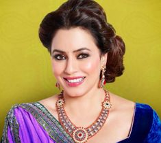 a woman in a purple and blue sari with jewelry on her neck, smiling at the camera