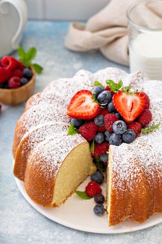 a cake with berries and powdered sugar on top sits on a plate next to a glass of milk