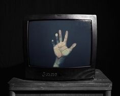 an old television with the hand on it's screen in front of a black background