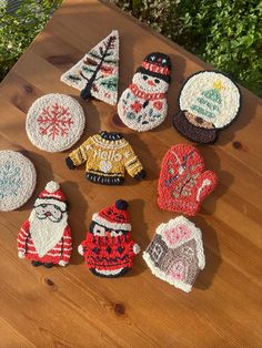 six knitted christmas ornaments sitting on top of a wooden table next to trees and snowmen