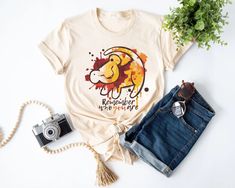 a t - shirt with a lion on it next to jeans and a camera