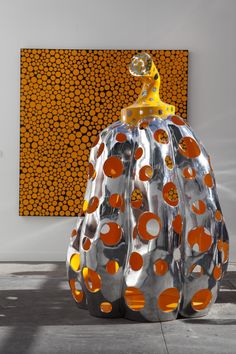 a large metal pumpkin sitting on top of a cement floor next to a yellow and orange painting