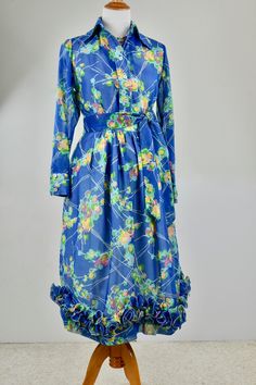 This sheer blue wrinkle reistant fabric is brought to life with abstact flowers in summer colors. The two piece dress has a matching tie belt and polyester accordion pleated and wired ruffled hemline. The top has a tailored blouse design with shell button down front. The blouse is not lined, the skirt has a white cotton blend lining. Skirt closes with hooks,eyes, and nylon zipper. ROMANTIC, FEMININE WRINKLE RESISTANT so GREAT CHOICE FOR EVENINGS OUT, PARTIES, TRAVEL, RESORTDUST OFF YOUR WHITE SA 1970s Style Blue Floral Print Dresses, 1970s Style Silk Dresses For Spring, Tailored Blouse, Blue Gown, Tie Dress, Two Piece Dress, Blouse Design, Summer Colors, Piece Dress