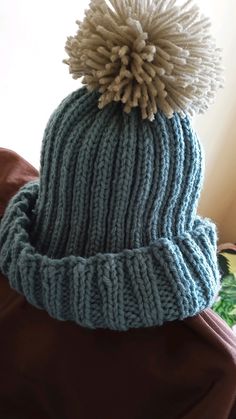 a blue hat with a white pom - pom on it sitting on top of a bed