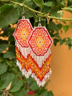 an orange and white beaded earrings hanging from a tree branch with leaves in the background