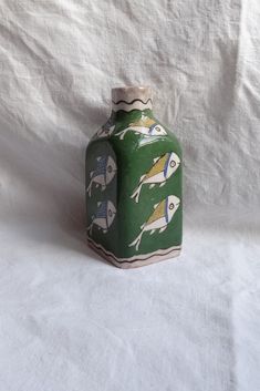 a green vase with fish painted on the front and sides, sitting on a white background