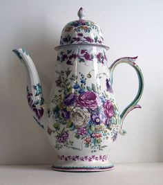 a teapot with flowers painted on it sitting on a table next to a wall