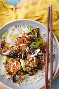 a white plate topped with meat and rice next to chopsticks