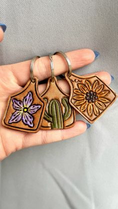 a person is holding three different keychains in their hand, one has a flower and the other has a cactus