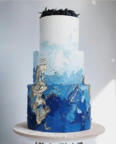 a three tiered blue and white cake with gold leaf decorations on it's top