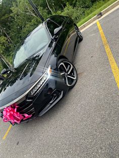 a black sports car with pink ribbon tied to it's hood parked on the side of the road