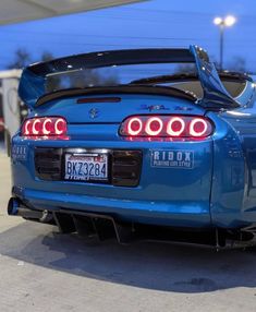 the rear end of a blue sports car parked in a parking lot with its lights on