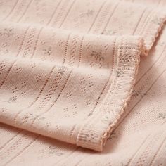 a close up view of a pink knitted blanket with small flowers on the edges