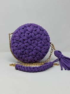 a purple crocheted purse with tassels and a chain around the strap