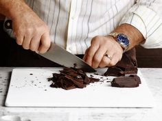 a man cutting up chocolate on top of a white cutting board next to a knife