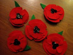 four red felt flowers with green leaves on a wooden table