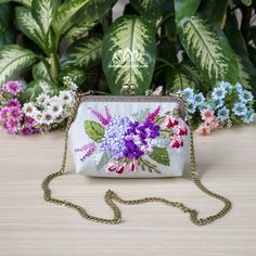 a purse with flowers painted on it sitting in front of some green leaves and plants