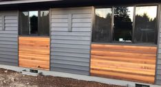 the side of a house with wood siding on it and windows in front of it