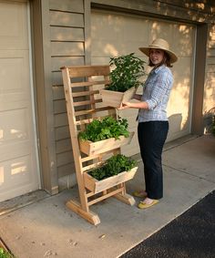 a woman standing next to a wooden planter filled with green plants in front of a garage