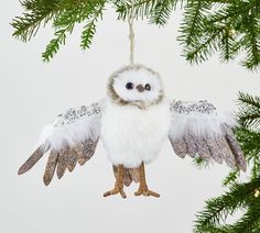 a white owl ornament hanging from a christmas tree with its wings spread out