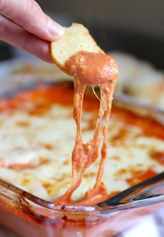 a hand holding a piece of bread and dipping it into a bowl of cheese dip