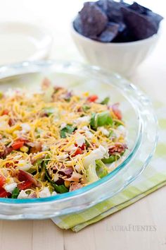 a glass bowl filled with salad next to a bowl of tortilla chips on a table