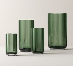 four green glass vases sitting next to each other on a white surface with no one around them