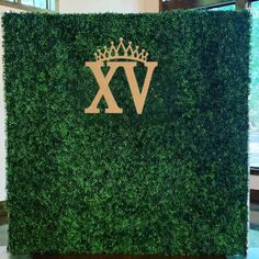 a tall green boxwood hedge with a crown on it's head and the letter v in gold