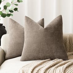 two pillows sitting on top of a couch next to a vase with green leaves in it