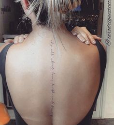 the back of a woman's neck with a tattoo on her left shoulder and words written in cursive writing