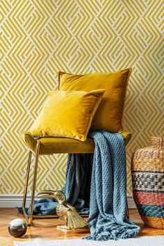 a yellow chair with two pillows on it next to a rug and a wallpaper