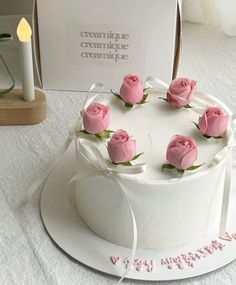 a white cake with pink roses on top sitting next to a lit candle and card