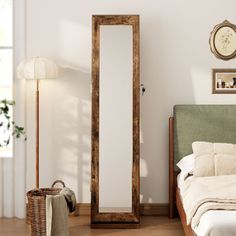 a bed sitting next to a tall wooden mirror in a bedroom on top of a hard wood floor