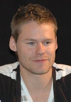 a close up of a person wearing a black vest and white shirt with his hair pulled back