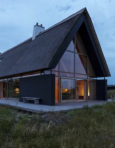 a house with a thatched roof and glass windows on the outside, at dusk