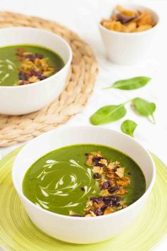 two white bowls filled with green soup on top of a plate